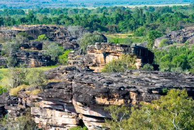 Elevated view of layered sandstone cliffs and scattered green trees in the Ubirr area of Kakadu National Park, Northern Territory, Australia.