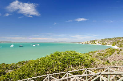 Elevated view across Kraalbaai in West Coast National Park, showing turquoise lagoon waters, anchored boats, white sand shoreline and coastal fynbos under a clear blue sky.