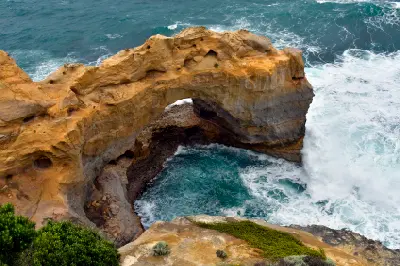 Close elevated view of The Arch with turquoise water swirling beneath the limestone formation in Port Campbell National Park.