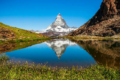 Matterhorn reflected in Riffelsee with clear water and alpine shoreline, Zermatt, Switzerland.