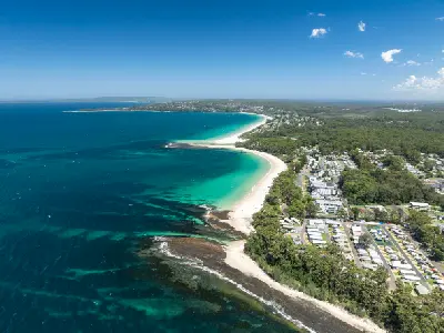 Aerial view along the white-sand beaches of Huskisson and Vincentia, with turquoise shallows, rocky reefs and the deep blue waters of Jervis Bay.