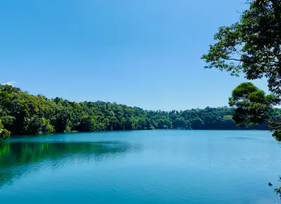 Wide view across the blue waters of Lake Eacham towards dense tropical rainforest beneath a clear sky in Queensland, Australia.