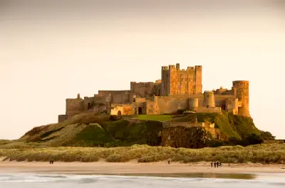 Bamburgh Castle overlooking the beach and sand dunes on the Northumberland coast of England at dusk.