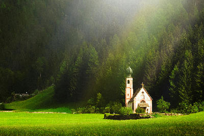 St. Johann in Ranui Church surrounded by green fields and forest in Val di Funes, Dolomites, Italy.