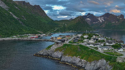 Aerial view of Husøy village on island in Øyfjorden, Senja Norway, showing coastal houses, harbour and mountains around the fjord.