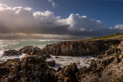 Dramatic storm clouds above the rocky coastline at De Kelders with crashing Atlantic waves and rugged cliffs in the Western Cape, South Africa.