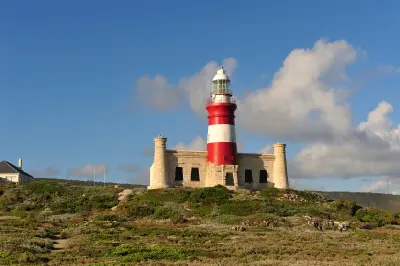 Red-and-white Cape Agulhas Lighthouse rising above coastal fynbos beneath blue skies in South Africa.