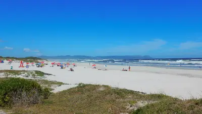 Wide sandy shoreline and ocean waves at Grotto Beach in Hermanus, South Africa, with beachgoers, coastal dunes, and views across Walker Bay on the Whale Coast.