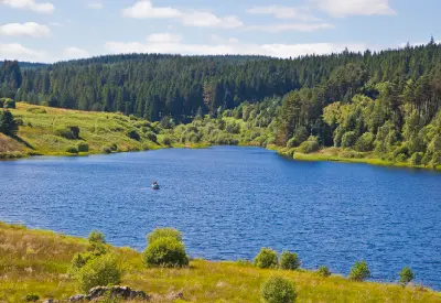 Blue waters of Kielder Reservoir surrounded by dense conifer forests and green hills in Northumberland, England, with a small boat on the lake.