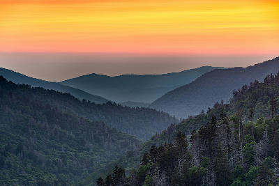 Layered mountain ridges at sunset viewed from Newfound Gap in Great Smoky Mountains National Park with orange skies and forested valleys.