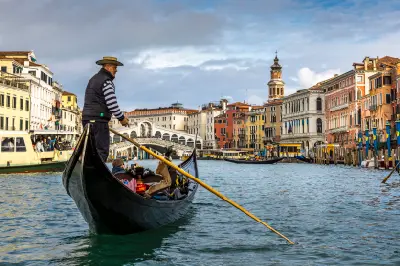 Rialto Bridge spanning the Grand Canal in Venice, with a gondolier in the foreground.