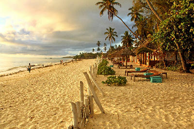 Sunrise over Jambiani Beach with white sand, palm trees, beachfront lodges, and calm Indian Ocean, Zanzibar, Tanzania.