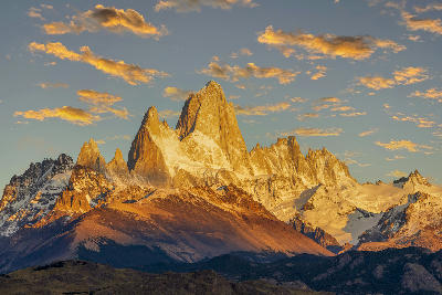 Mount Fitz Roy glowing in warm sunrise light with surrounding peaks and clouds in Patagonia, Argentina.