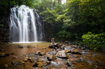 Ellinjaa Falls flowing into a rainforest pool, with a fallen tree, scattered boulders and a rocky creek in the Atherton Tablelands, Queensland.