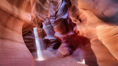 Light beams inside Upper Antelope Canyon in Arizona, showing smooth curved sandstone walls and a narrow slot canyon with illuminated sand floor.