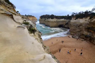 Visitors on the beach inside Loch Ard Gorge beneath towering limestone cliffs in Victoria, Australia.