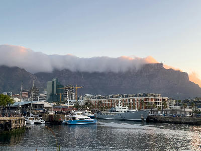 Boats and yachts at the V&A Waterfront harbour with Table Mountain and cloud cover at sunset in Cape Town, South Africa.