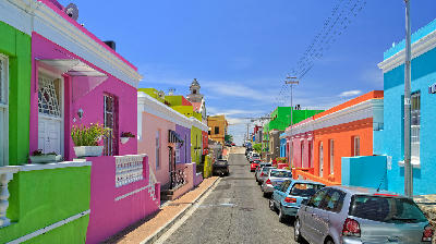 Colorful historic houses along a sloping street in Bo-Kaap with parked cars and clear blue sky, Cape Town, South Africa.