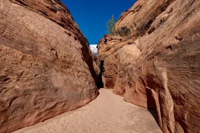 Narrow entrance to Spooky Gulch, with smooth red sandstone walls closing around a sandy passage beneath a deep blue sky.