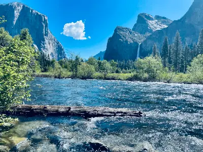 Merced River flowing across the Yosemite Valley floor with granite cliffs and a waterfall in Yosemite National Park, California.