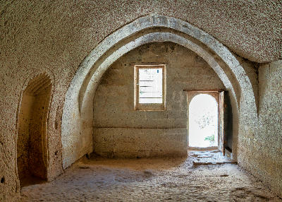 Interior of the rock-cut mosque at Zelve Open Air Museum with vaulted stone ceilings, arched doorway and carved volcanic tuff walls in Cappadocia, Turkey.