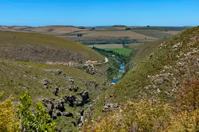 River gorge and winding road through Tradouw Pass surrounded by rolling hills and farmland in the Western Cape, South Africa.