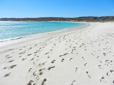 Footprints cross the white sand beside clear turquoise water at Turquoise Bay.