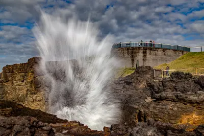 A powerful burst of seawater erupts from the Kiama Blowhole as visitors watch from viewing platforms above the rocky coastline.