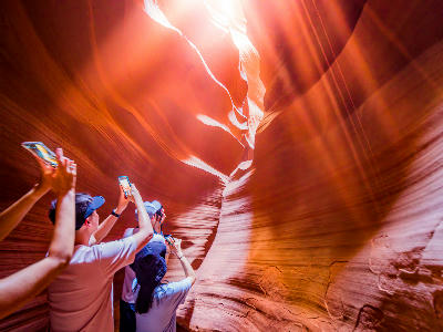 Visitors photographing light entering Upper Antelope Canyon through narrow sandstone walls