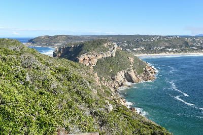 View from Robberg Peninsula across rocky coastal cliffs, fynbos-covered slopes and the waters of Plettenberg Bay in South Africa.
