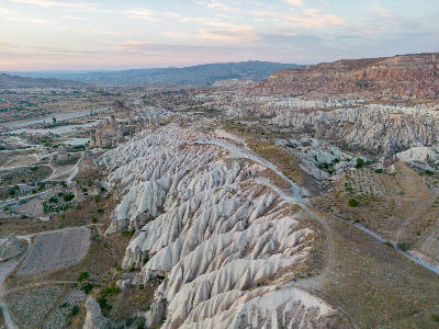 Aerial panorama of Red Valley in Cappadocia, Turkey, showing eroded volcanic ridges, fairy chimneys, winding tracks, and layered rock formations at sunset.