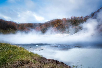 Steam rising from the surface of Oyunuma Pond surrounded by autumn forest in Noboribetsu, Hokkaido, Japan.
