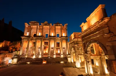 Illuminated façade of the Library of Celsus at Ephesus glowing against a deep blue night sky.
