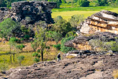 Walker among layered sandstone formations, rocky ledges and tropical woodland in the Arnhem Land region of Australia's Northern Territory.
