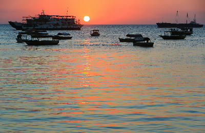 Boats silhouetted against a colourful sunset viewed from the Forodhani Gardens waterfront in Stone Town, Zanzibar.