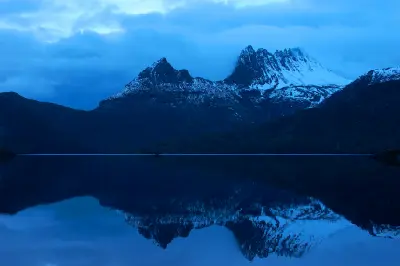 Snow-covered Cradle Mountain reflected in Dove Lake beneath low clouds in Tasmania, Australia.
