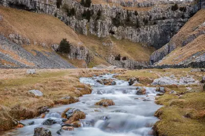 Long-exposure view of Gordale Beck flowing over rocks towards the limestone cliffs and narrow gorge of Gordale Scar, North Yorkshire.