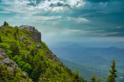 Rocky cliffs and evergreen slopes on Grandfather Mountain overlooking layered Blue Ridge Mountains beneath dramatic storm clouds.
