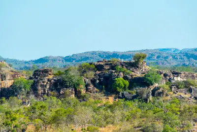 Layered sandstone cliffs surrounded by tropical woodland with distant escarpment ridges in Arnhem Land, Northern Territory, Australia.