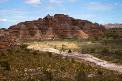 Striped sandstone domes of the Bungle Bungle Range rise above a dry creek bed and sparse Kimberley bushland.