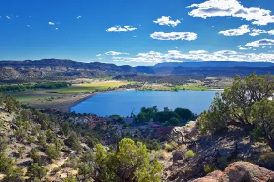 Panoramic view over Wide Hollow Reservoir, surrounded by juniper-covered hills, green fields and layered desert mesas near Escalante.