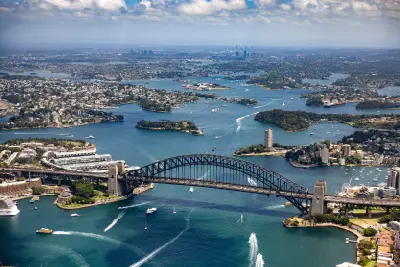 High aerial view across Sydney Harbour with the Harbour Bridge, ferries, islands and waterways stretching towards the western suburbs.