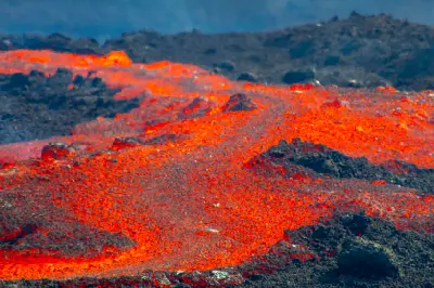 Bright orange lava flowing across black volcanic rock at Fagradalsfjall eruption site on the Reykjanes Peninsula, Iceland.