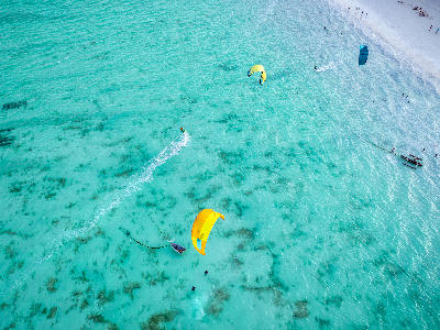 Drone view of colourful kitesurfers gliding across the shallow turquoise lagoon at Paje Beach, Zanzibar, Tanzania.