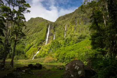 Poço da Ribeira do Ferreiro (Poço da Alagoinha) on Flores Island, with multiple waterfalls cascading down lush green cliffs into a natural lagoon in the Azores