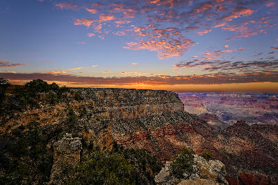 Grand Canyon South Rim at sunset with rim-edge cliffs and layered canyon formations under a colourful sky