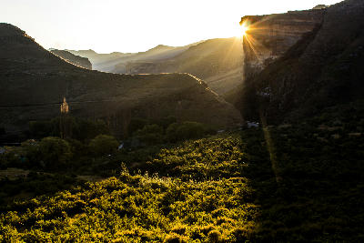 Sun rays bursting from behind Brandwag Buttress at sunset, illuminating the valley and sandstone cliffs of Golden Gate Highlands National Park in the Free State, South Africa.