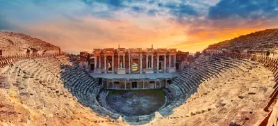 Panoramic view of the ancient Roman Theatre of Hierapolis, with its tiered stone seating and monumental stage façade beneath a dramatic sunset sky.