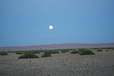 Moon above open gravel plains and distant desert dunes in the Namib Desert near Sesriem, Namibia.