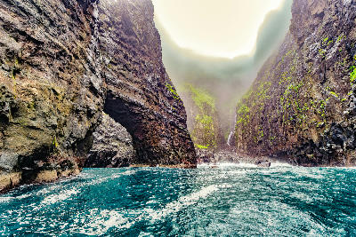 Boat-level view beneath a basalt sea arch inside the Vestmanna bird cliffs with steep canyon walls and turquoise water, Streymoy, Faroe Islands.